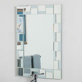 A bathroom mirror framed by square glass tiles, reflecting the surrounding space.